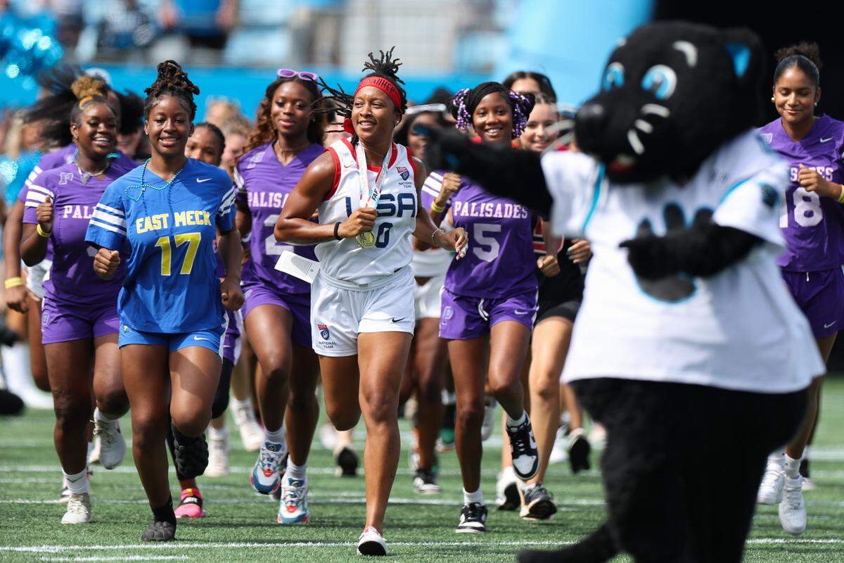 Amber Clark, center, a North Carolina native and gold-medal winning USA Football flag football athlete, leads a group of CMS flag football-playing girls out of the tunnel at Saturday's Panthers game in Bank of America Stadium on August 12, 2023.