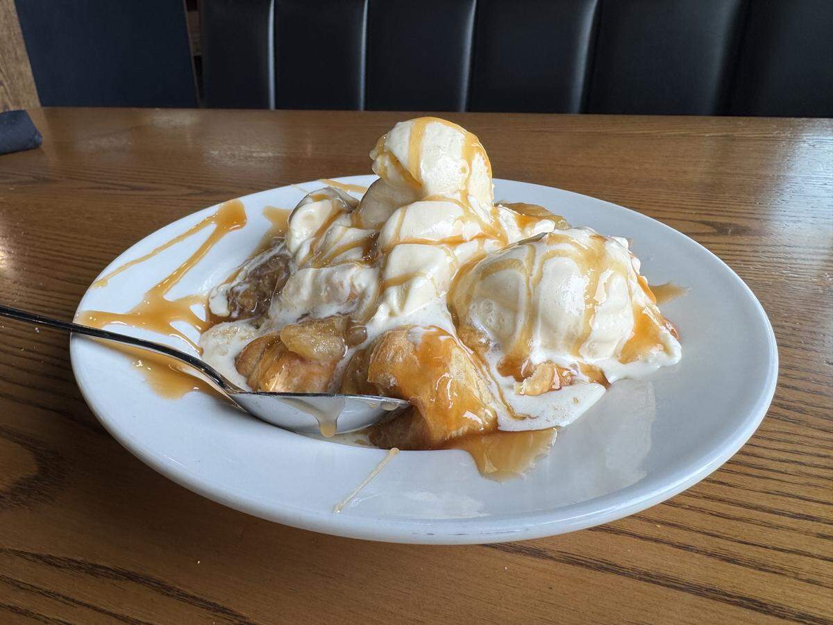 A decadent dessert consisting of warm pastry or cobbler topped with three large scoops of melting vanilla ice cream, all generously drizzled with golden caramel sauce.