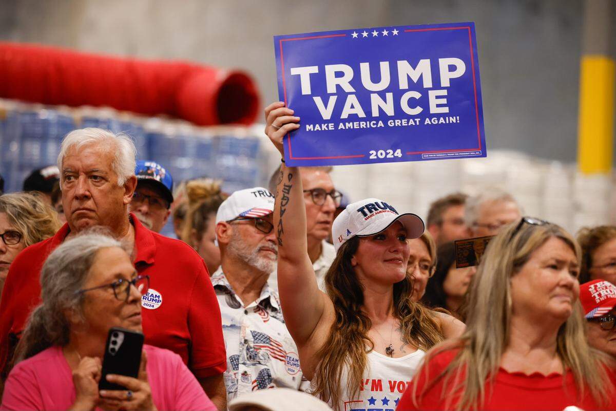 Supporters of Former President Donald Trump hold up signs and wear branded apparel during a campaign rally inside the Mosack Group manufacturing warehouse in Mint Hill, NC on Wednesday, September 25, 2024.