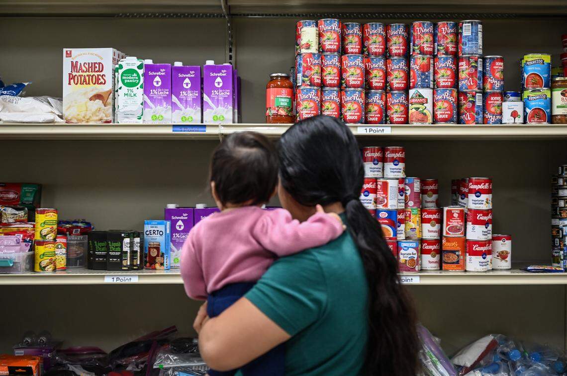 A mother holds her infant as she shops for food at the pantry at Care Ring on Plymouth Avenue in Charlotte, NC on Thursday, October 31, 2025. Care Ring is a nonprofit organization dedicated to providing health services for the uninsured, underinsured or those lacking access to affordable, high-quality health care through its Care Ring Clinic and Physicians Reach Out network.