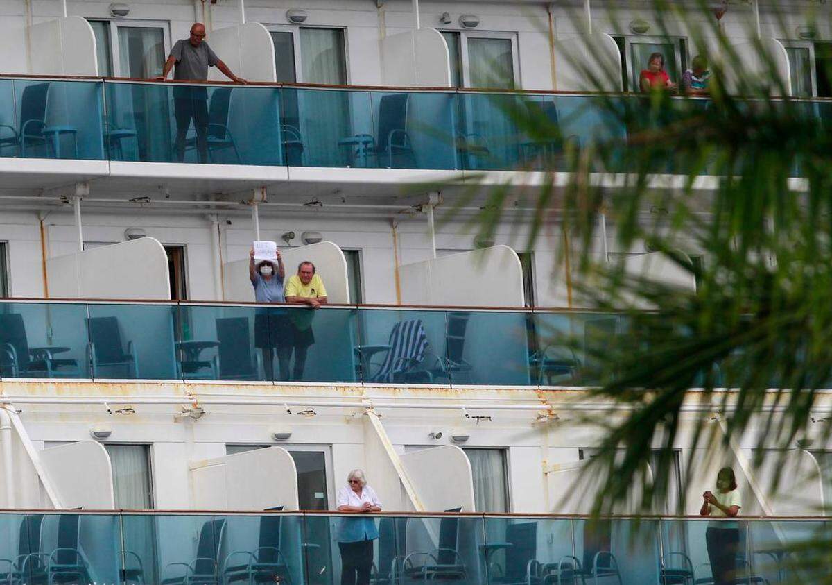 A Coral Princess passenger holds up a sign that reads “Let Me Go” as she and another passenger stand on their balconies on Sunday.