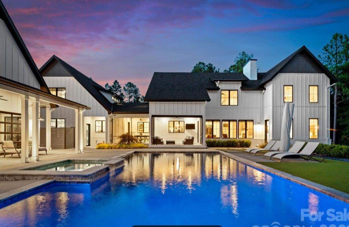 Outside the home is this in-ground pool, along with a covered dock and a pool house whose garage-style doors open to a pool deck, a full bar and a golf simulator screen.