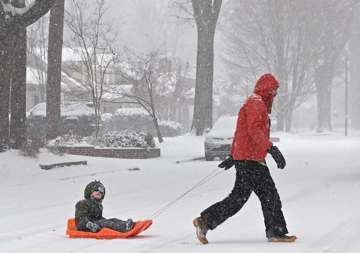 As the snow falls, Jonathan Boone, right and son, Avett, left make their way along Lyon Court in Charlotte, NC on Saturday, January 31, 2026.