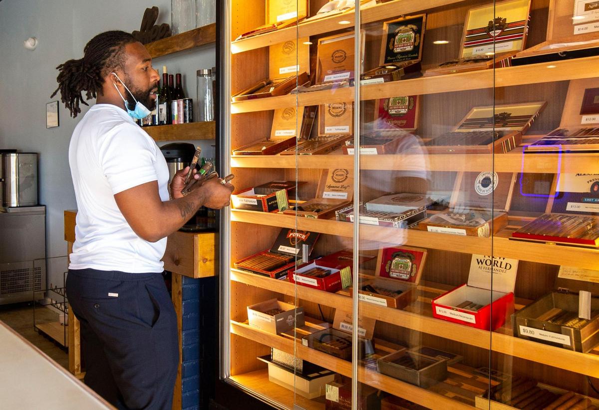 Co-owner Xavian Seiferth selects a variety of cigars from the display case at Sticks and Beans.
