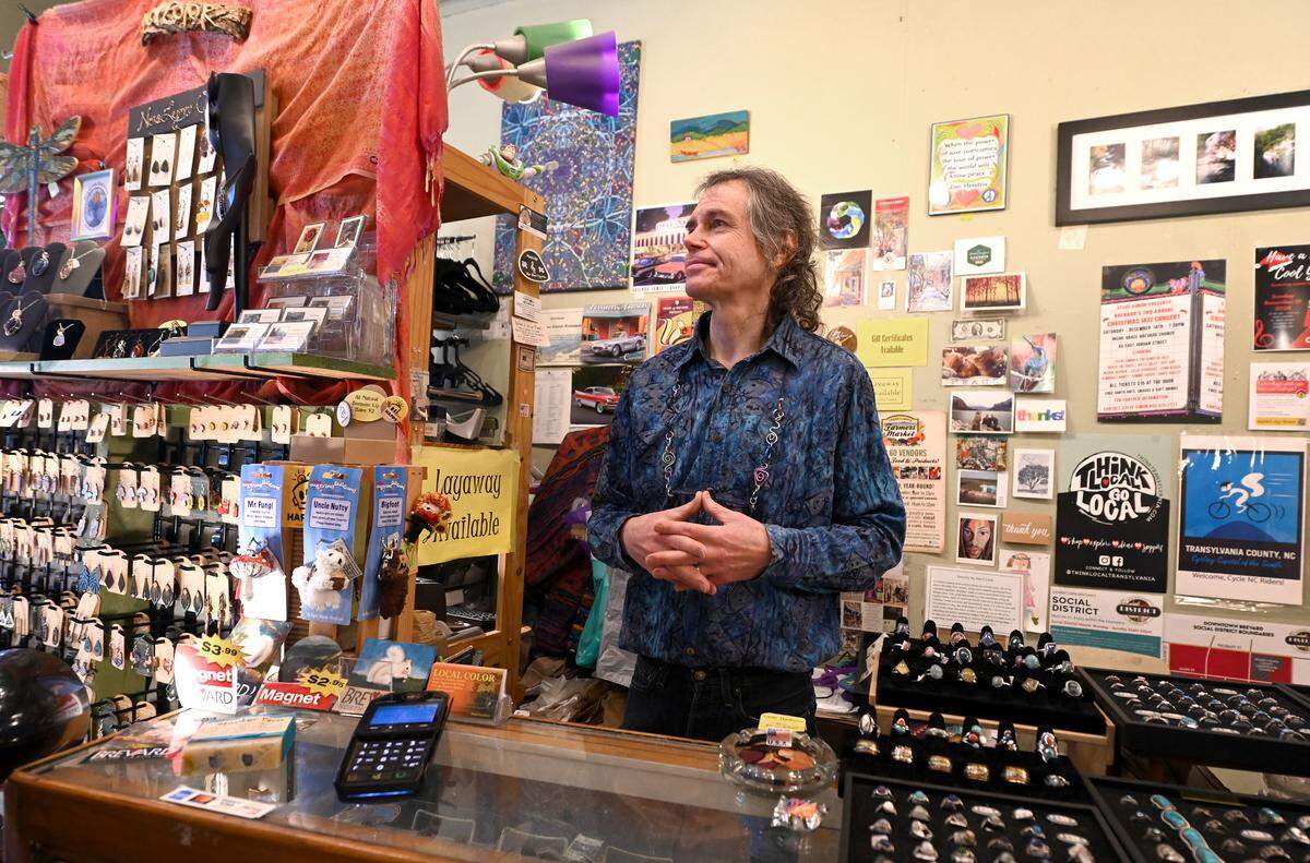 Paul Hawkins, the owner of Local Color in Brevard, NC stands behind the counter on Friday, November 15, 2024. Hawkins says that following Hurricane Helene his profits are down 40% compared to last year.