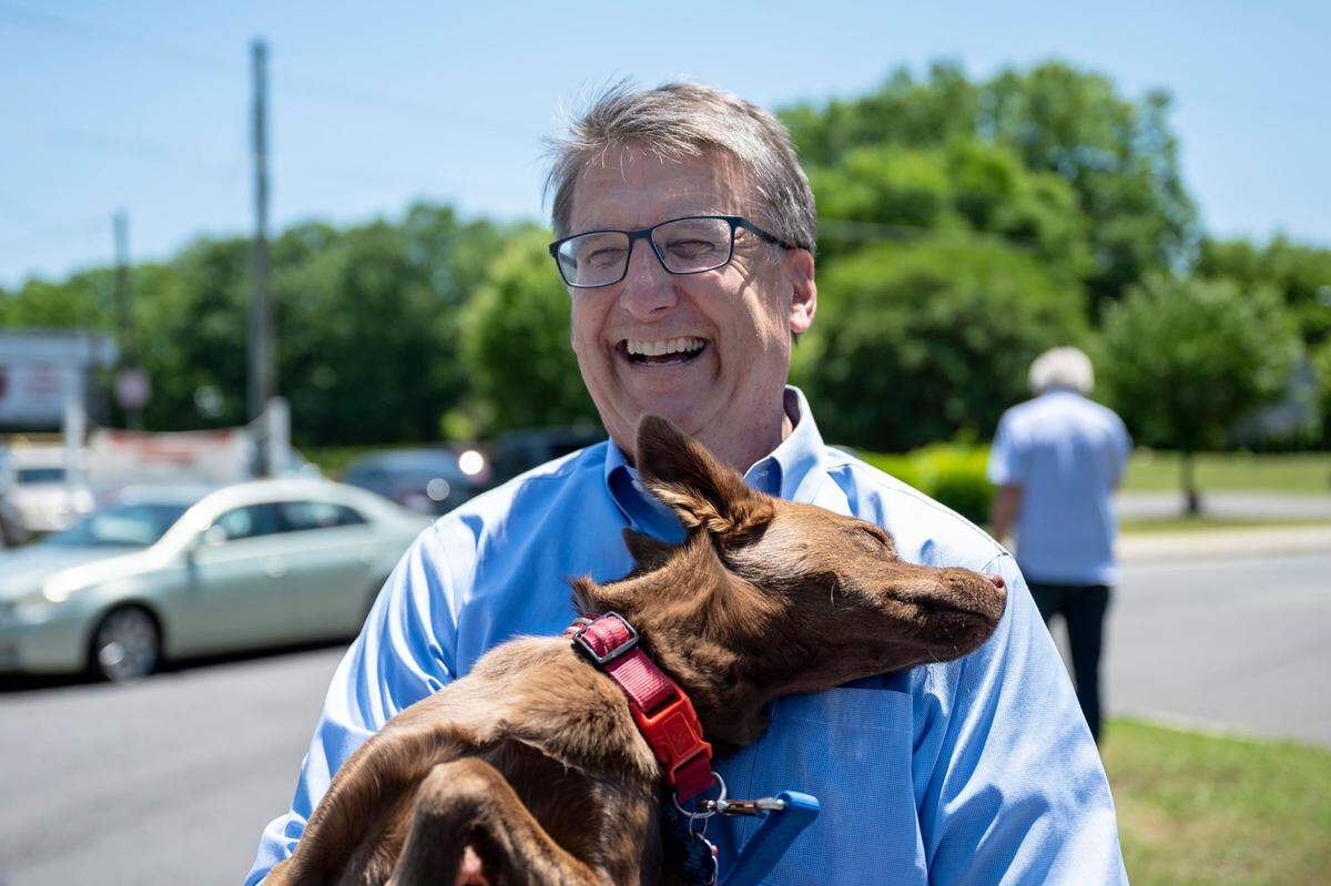 Former Gov. Pat McCrory, a Republican candidate for Senate, laughs as he holds his dog, Maddie, a rescue dog found running down Independence Boulevard, on Election Day outside of Alexander Graham Middle School on Tuesday, May 17, 2022 in Charlotte. Speaking about Maddie’s importance to his campaign, McCrory said “She’s going to help me rescue our democracy and the American dream.”