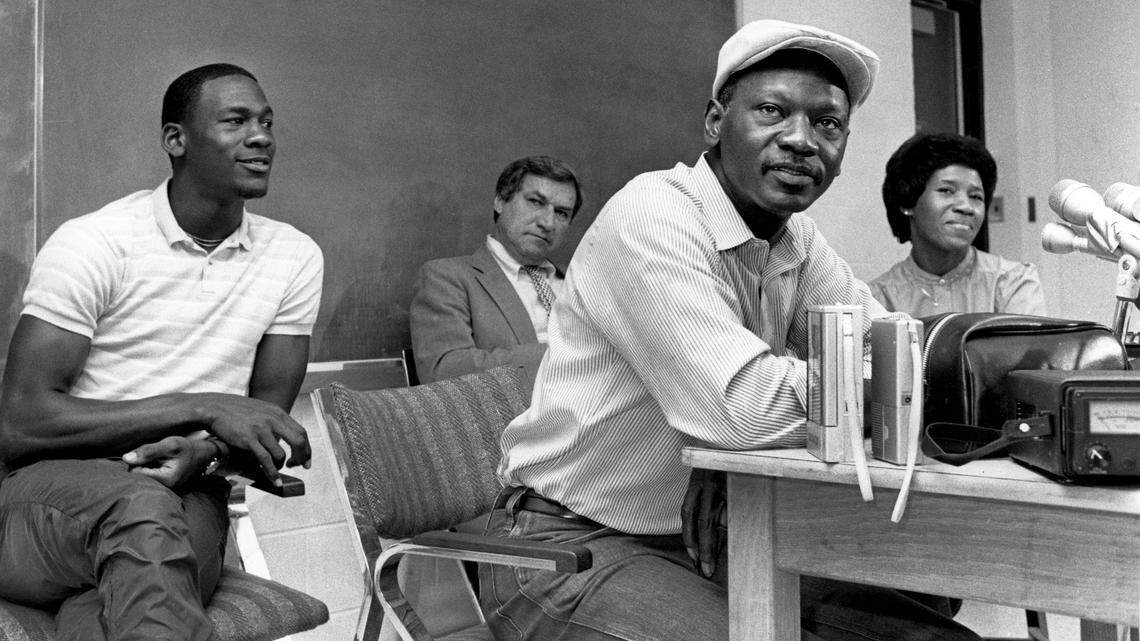 Michael Jordan (left) watches as his father James Jordan speaks with reporters at a press conference where he announced that he would leave the University of North Carolina early to enter the NBA draft. Jordan’s mother Delores is at right and coach Dean Smith is at center rear.
