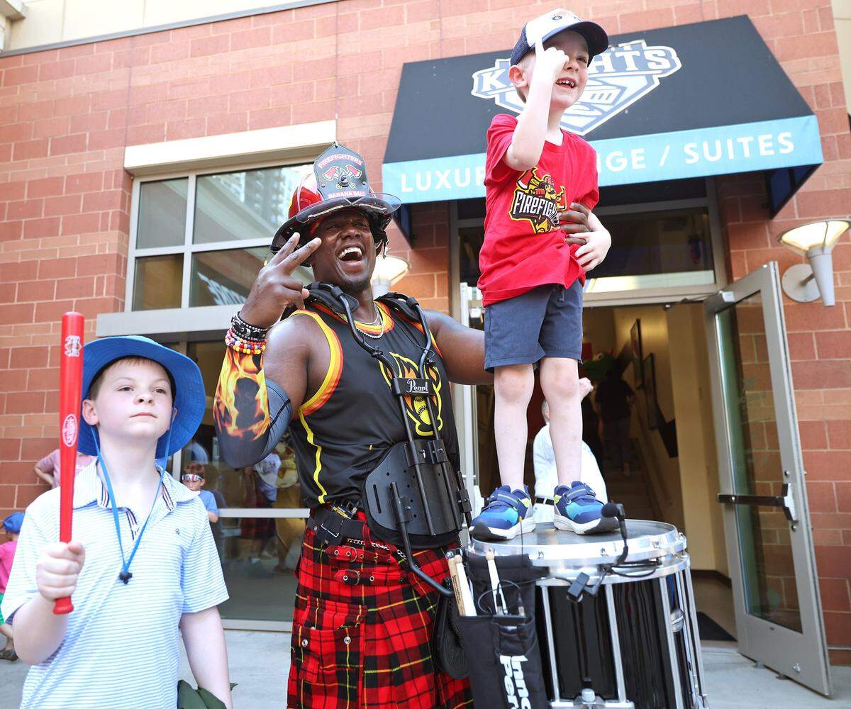 Fan Finley Hursey, 4 yrs. stands on the drum of Fireline member Smoke Stack as he and his brother, Owen Hursey, 11 yrs., pose for a photograph at Truist Field in Charlotte, NC on Thursday, June 4, 2026. Fans packed Truist Field for Banana Ball action between the Texas Tailgaters and Firefighters.