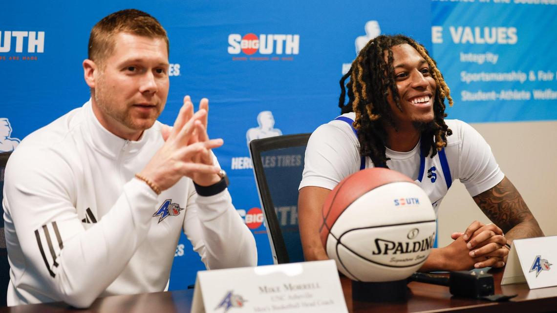 UNC Asheville guard Josh Banks, right, smiles as head coach Mike Morrell speaks during the Big South media day in Charlotte, NC on Tuesday, Oct. 15, 2024.