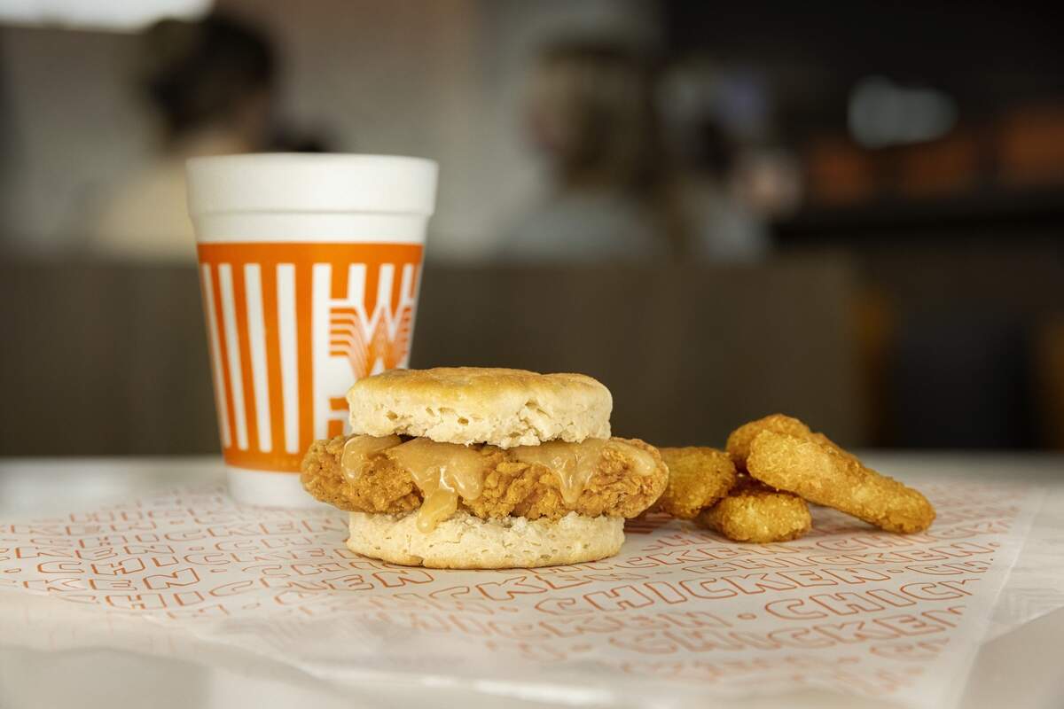A Whataburger Honey Butter Chicken Biscuit served on branded paper wrapper next to crispy hash brown sticks and an orange-and-white striped cup.