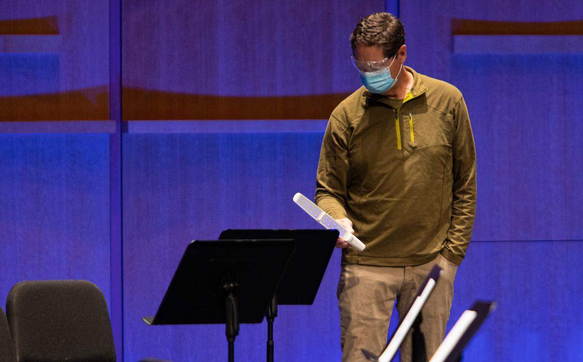 The Charlotte Symphony Orchestra has restarted indoor rehearsals and is taking many COVID-19-related precautions. Here, Stage Manager John Jarrell goes over every surface with a UV light to kill germs at the Knight Theatre, where the group rehearsed. Musicians and others must fill out a questionnaire and get temperature checks upon arrival.