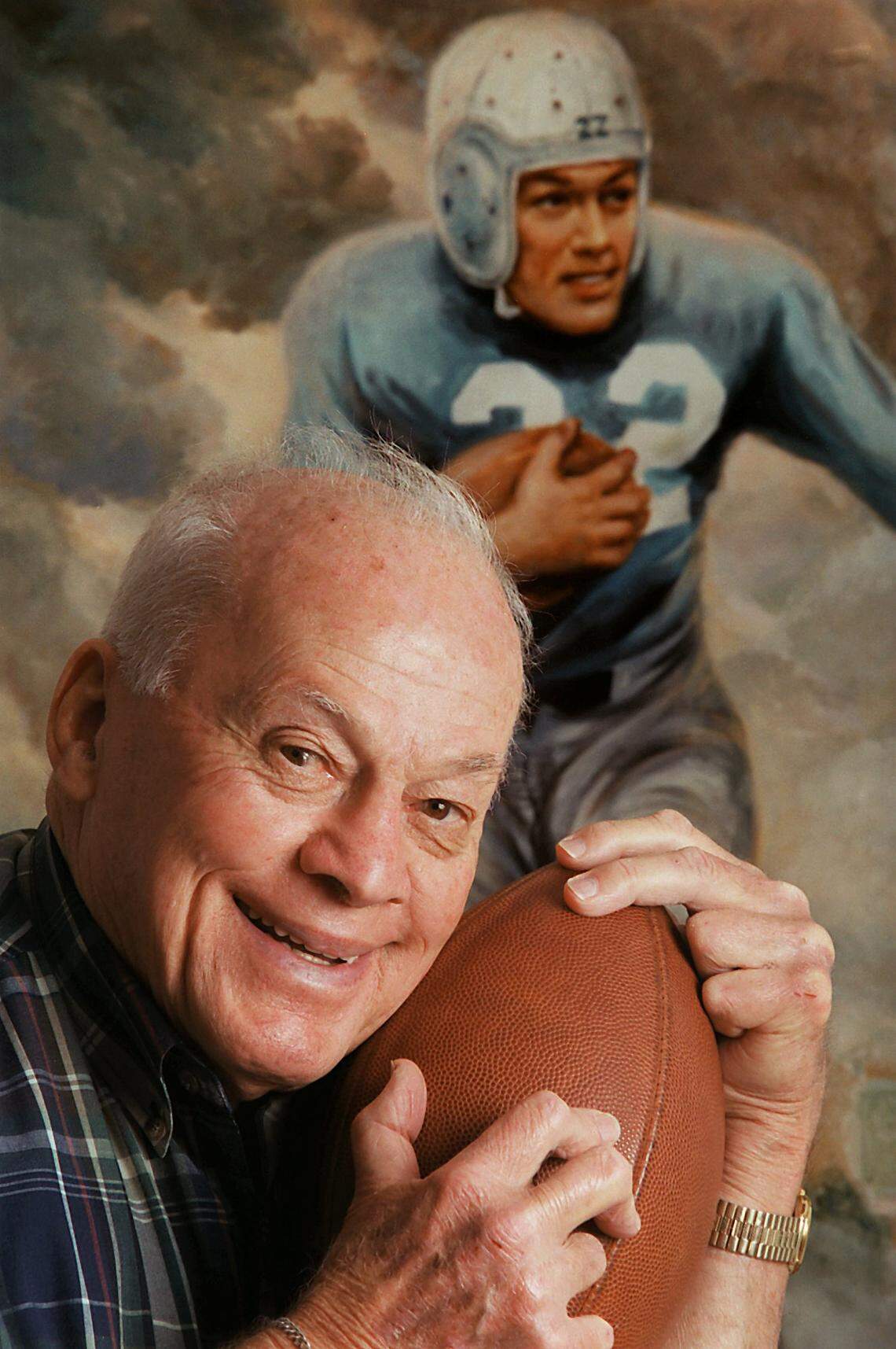 In 2000, Charlie “Choo Choo” Justice posed with a football and a painting of himself during his glory days at UNC at his home in Cherryville. Justice died in 2003.
