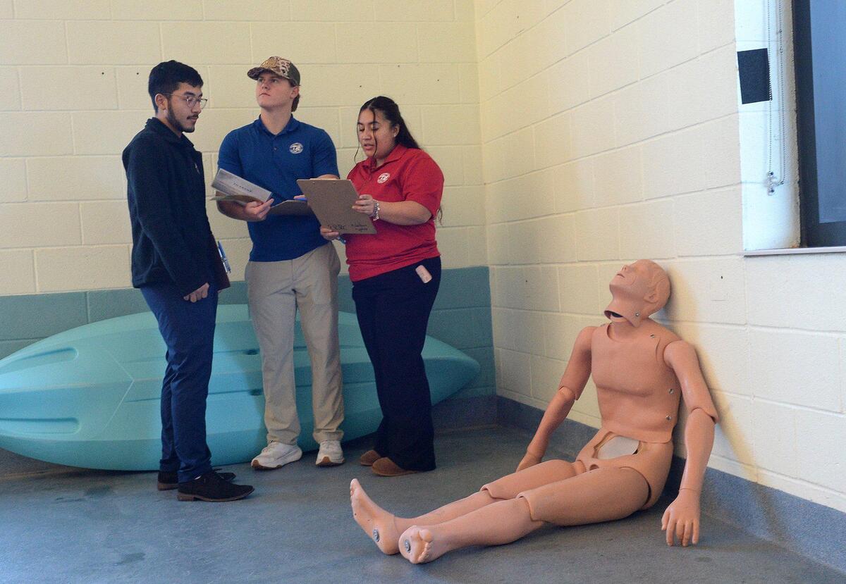 (L to R) Angel Cabrera Paulino, 20, Peyton Mincey, 21 and Angelica Cabrera , 23, huddled in the corner of the lap pool at Eastway Regional Recreation Center trying to find clues to a murder mystery hidden in and around the pool. A Mecklenburg County Park and Recreation department program entitled, Aquatic Mystery Solvers, gathered Aquatic Recruiting Team members to test drive the program on Saturday, Dec. 07, 2024. The program is open to folks ages 14-99, wishing to sharpen their in-water skills while finding clues to the mystery.