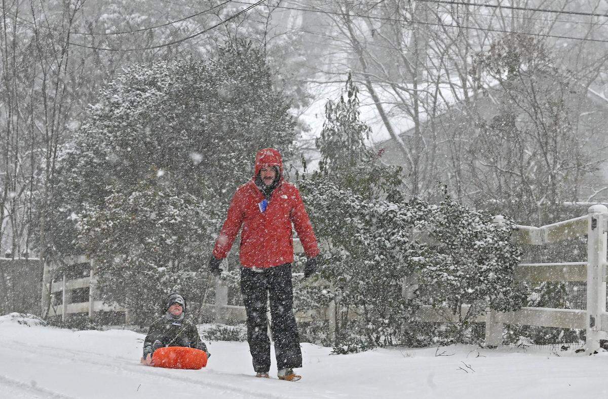 As the snow falls, Jonathan Boone, right and son, Avett, left make their way along Lyon Court in Charlotte, NC on Saturday, January 31, 2026.