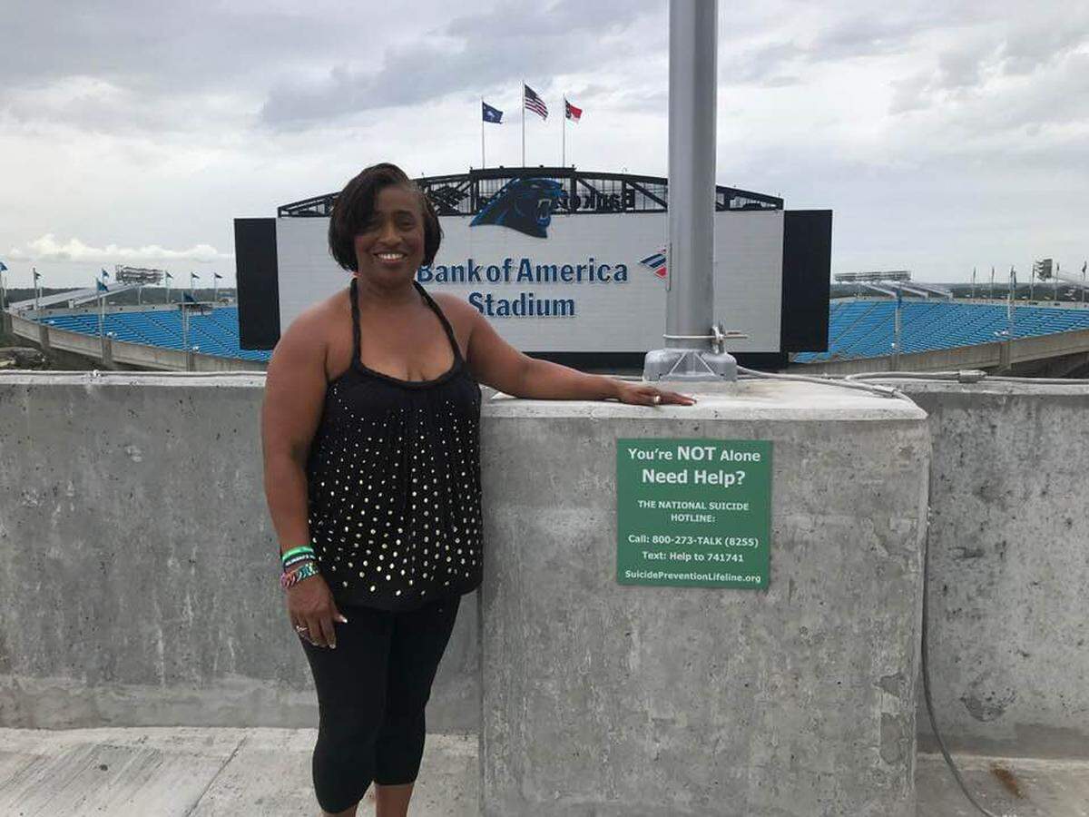 Fonda Bryant, a local mental health advocate, stands in front of a National Suicide Hotline sign posted near Bank of America Stadium. The number is 800-273-8255.