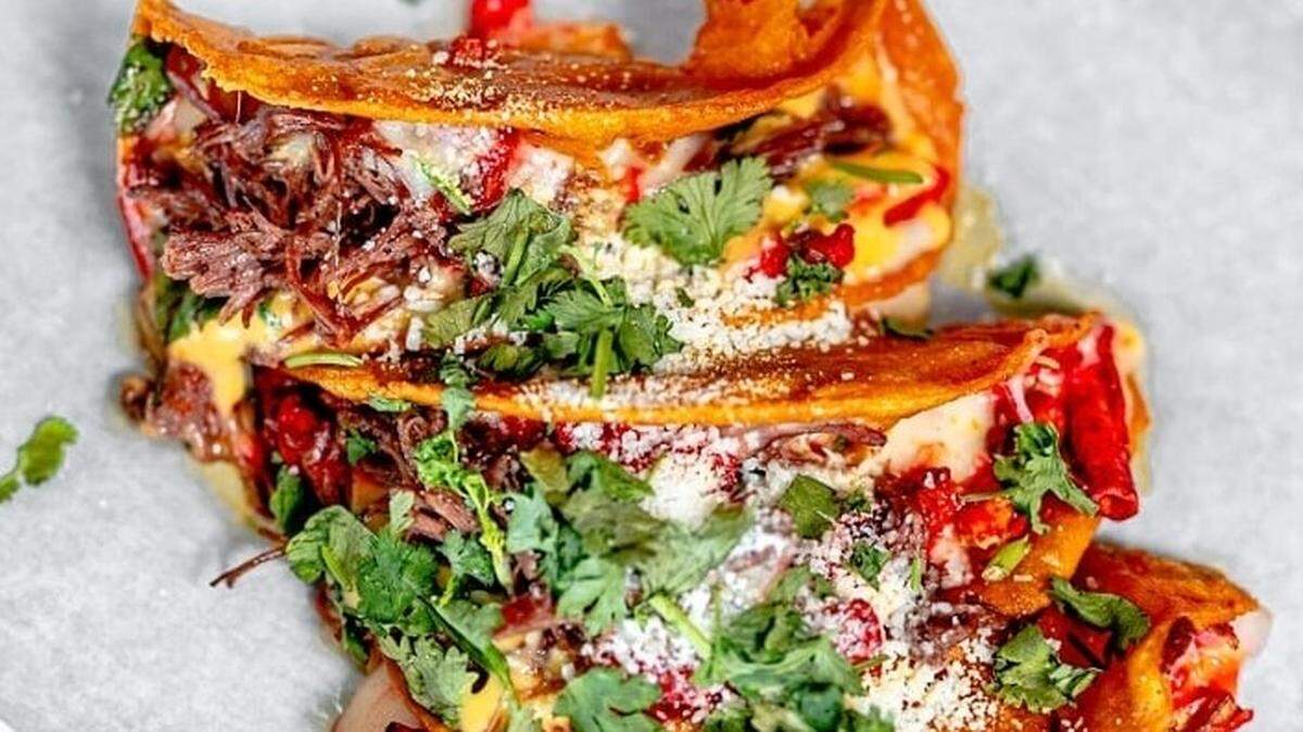 Talkin’ Tacos’ Birria Taki Tacos are made with birria and Chihuahua cheese, then topped with onion, cilantro, cheese sauce and crumbled takis on corn tortillas —and they’re served with consomme for dipping.