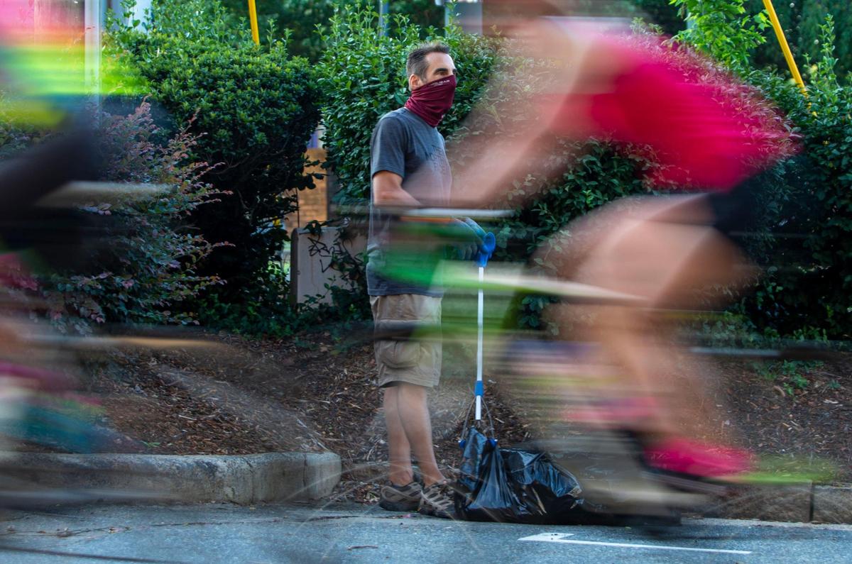 Paul Neumann watches cyclist ride by as he searches the bushes for trash along the Rail Trail in South End on Saturday, July 11, 2020. Neumann picks up trash along the trail and anywhere trash is hidden as part of his weekend run.