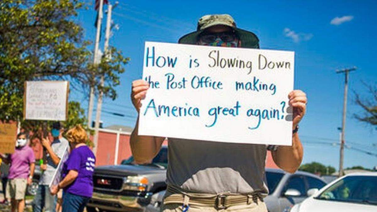 A few dozen protesters gathered Aug. 11 outside a post office in Midland, Mich. Eric Severson holds a sign to protest recent changes to the U.S. Postal Service under new Postmaster General Louis DeJoy.