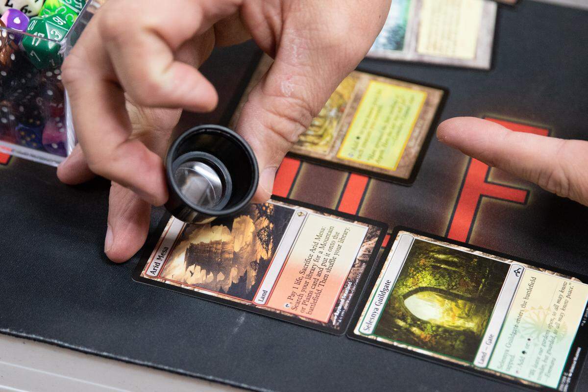 Leon Fortner uses a magnification lense to determine the validity and value of some “Magic: The Gathering” cards.