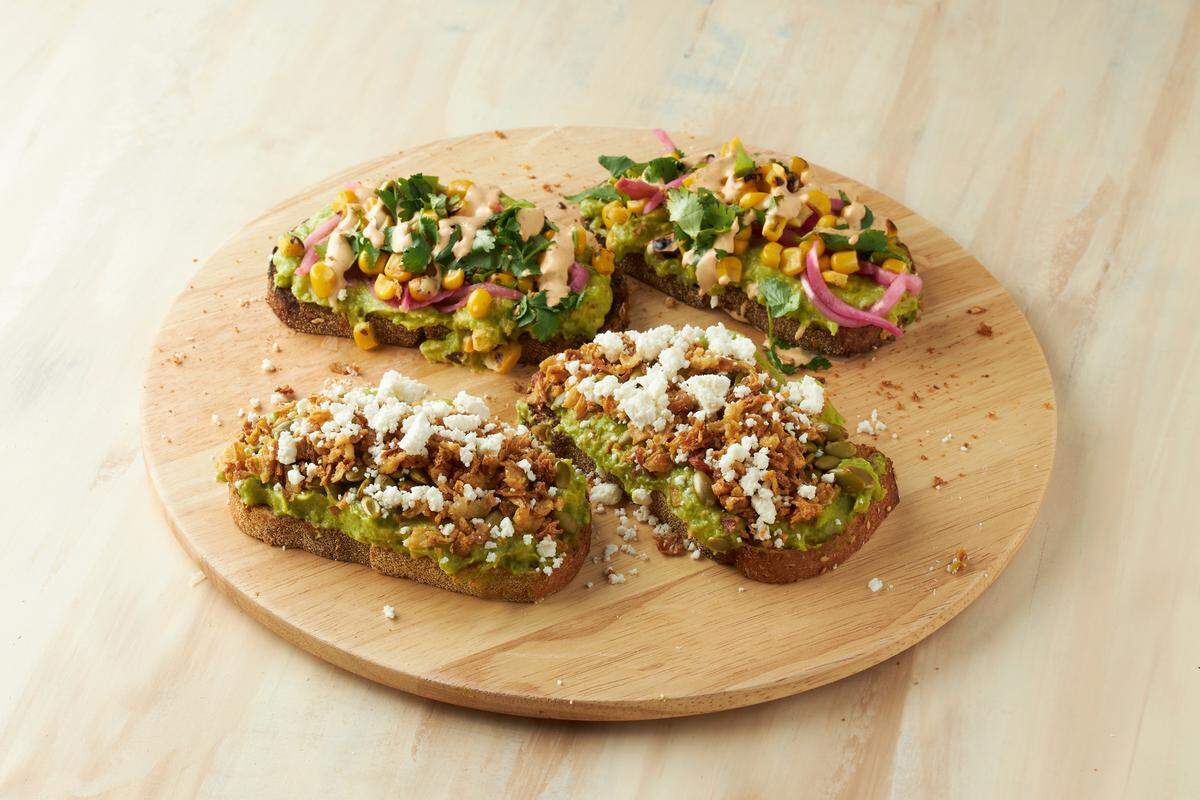 Avocado toast options at Just Salad include the Avo Blast Toast with corn, pickled red onions, cilantro and smoky poblano ranch and the Crunchy Avocado Toast with feta, roasted pumpkin seeds and crunchy onions.