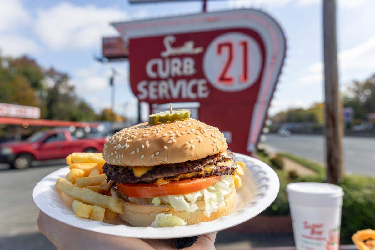 A stacked double bacon cheeseburger with a side of seasoned fries on a white plate.
