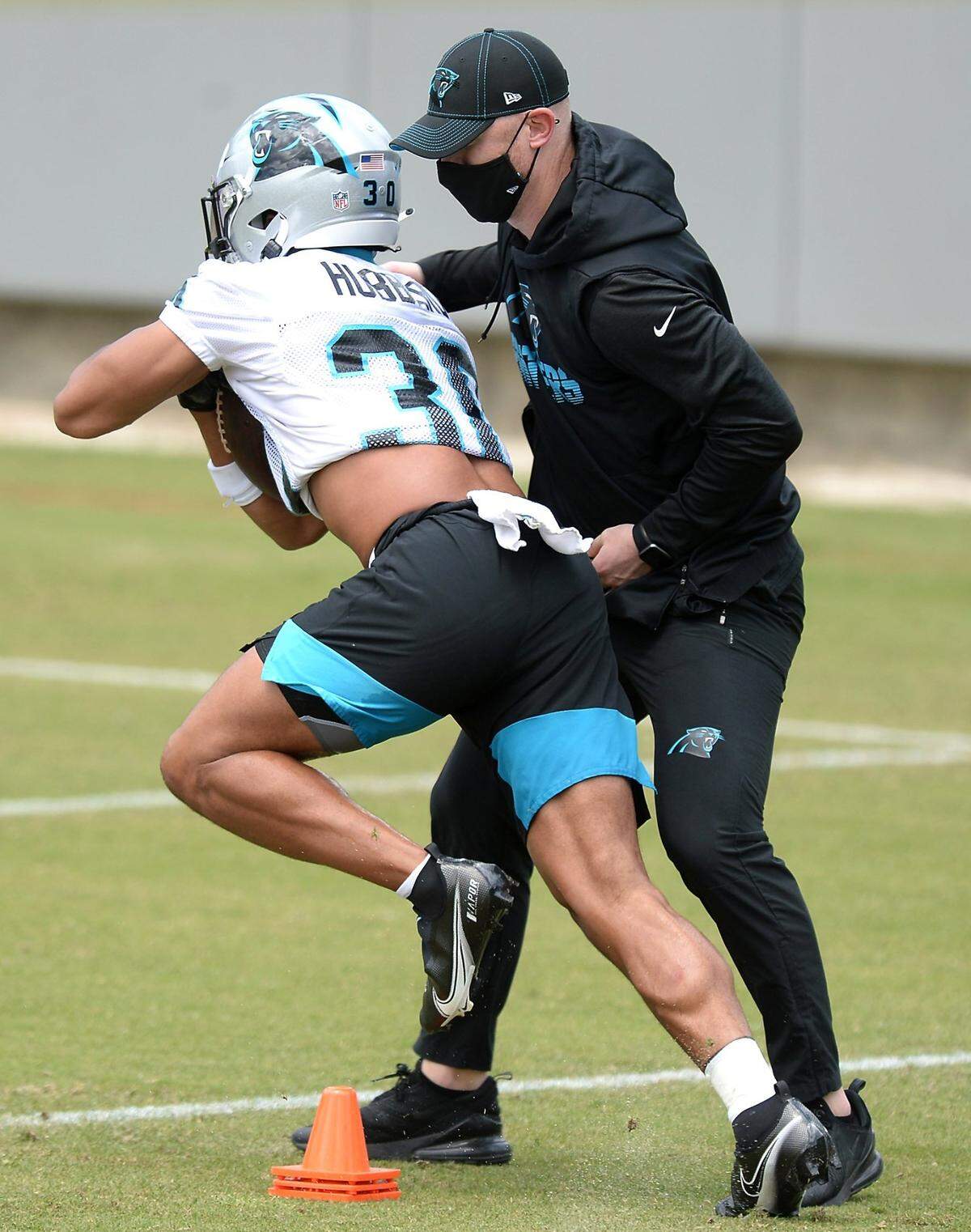 Carolina Panthers rookie running back Chuba Hubbard, left, continues to push himself upfield as offensive coordinator Joe Brady, right, attempts to strip the ball away during the team’s 2021 rookie minicamp practice on Friday, May 14, 2021.