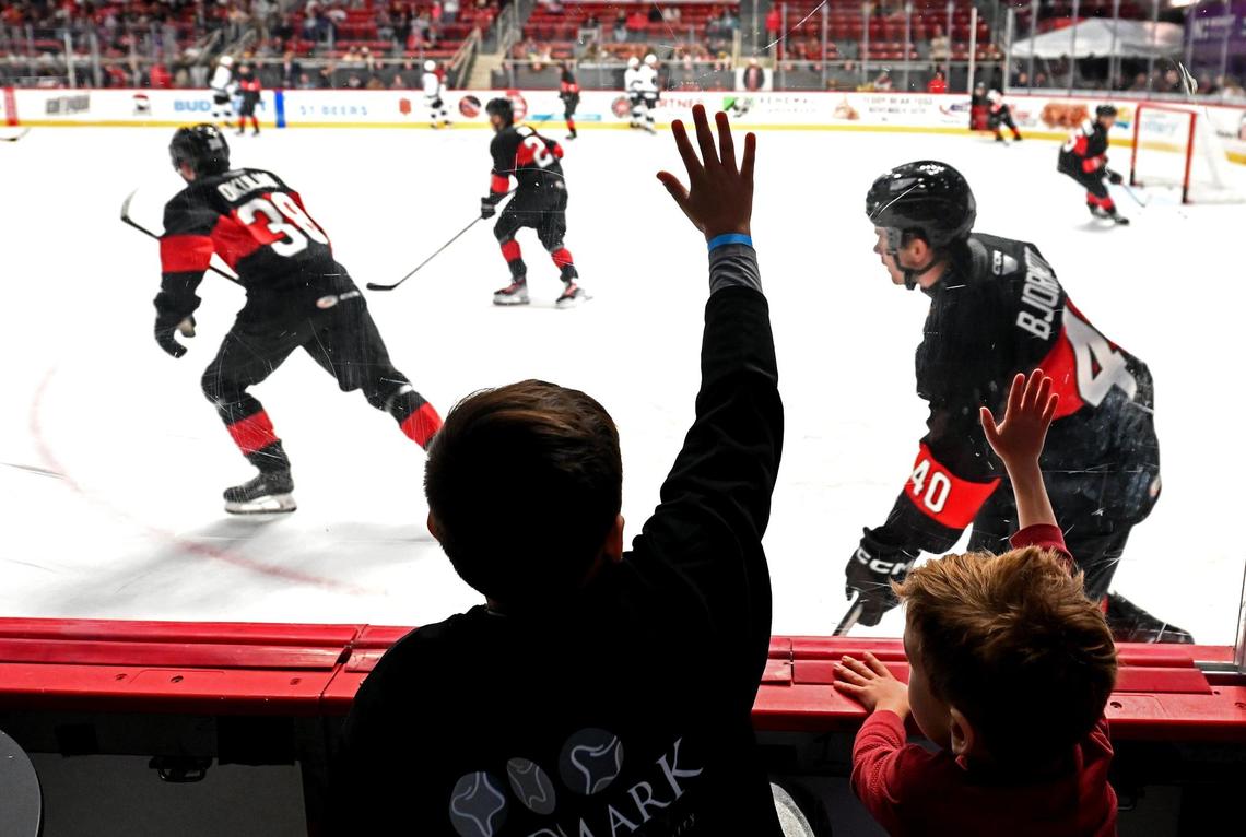 Charlotte Checkers fans Rocco Patel, left and Silas LeBlanc, right, try to get the attention of players as they warmup at Bojangles Coliseum in Charlotte, NC on Friday, October 18, 2024. The Charlotte Checkers hosted the Cleveland Monsters in the home opener.
