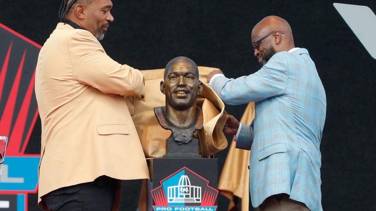 Aug 3, 2024; Canton, OH, USA; Julius Peppers (left) and his presenter Carl Carey (right) unveil the bust of Peppers as he is inducted into the Pro Football Hall of Fame at the enshrinement ceremony at Tom Benson Hall of Fame Stadium. Mandatory Credit: Charles LeClaire-USA TODAY Sports