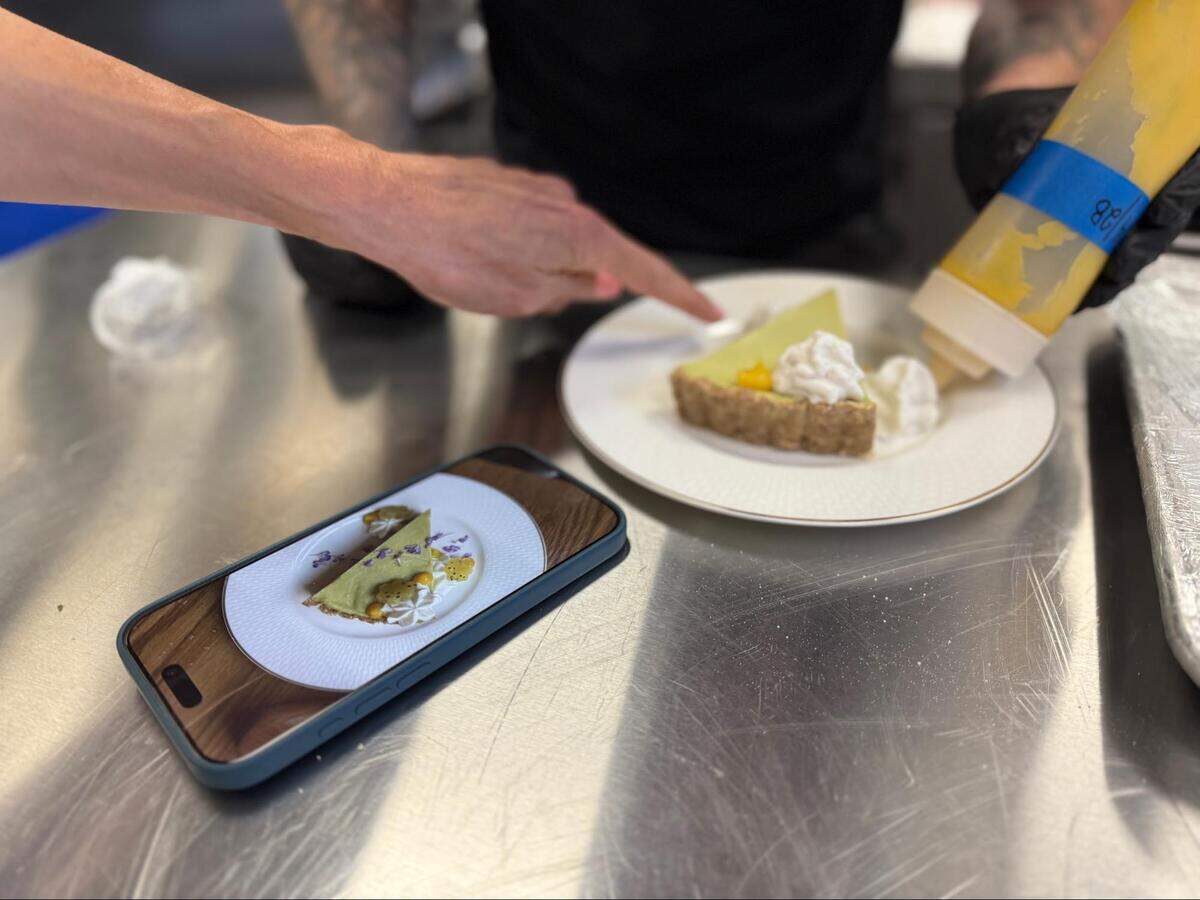 The kitchen crew members at Leluia Hall are still learning how to plate the avocado lime pie, so co-owner Jamie Brown uses a photo to guide sous chef Alex Zellers on how to get all of the details just right.