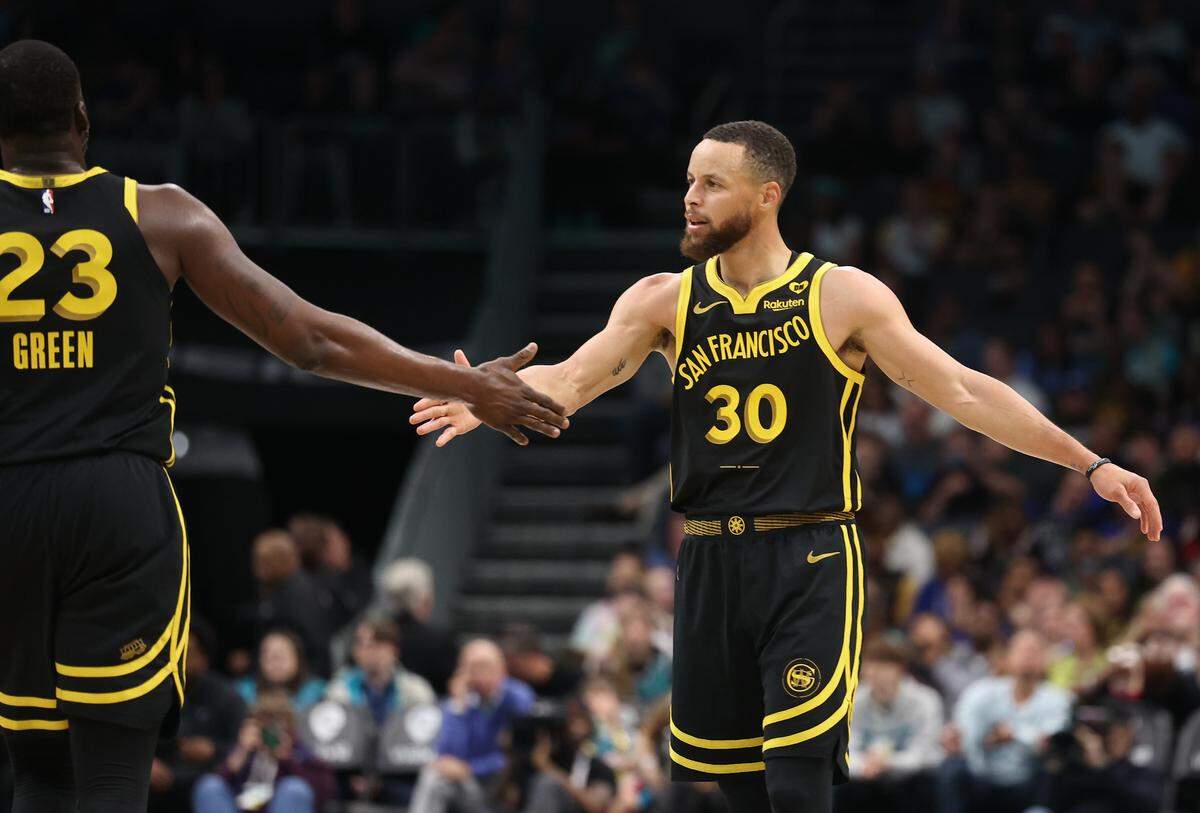 Golden State Warriors guard Steph Curry, right, reaches out to slap hands with teammate Draymond Green, left, following a play against the Charlotte Hornets during first quarter action at Spectrum Center in Charlotte, NC on Friday, March 29, 2024.