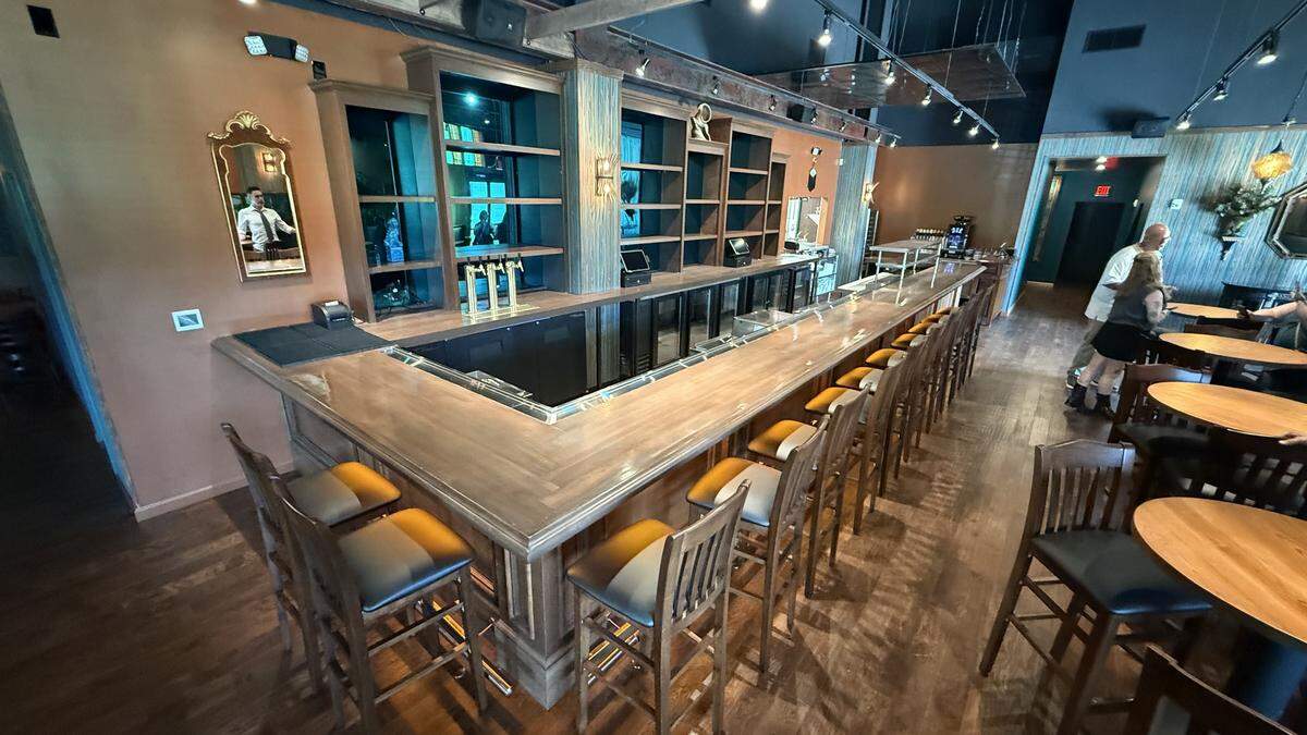 A wide shot of the long, polished wooden bar at Soul Gastrolounge, lined with dozens of bar stools. The extensive back bar is ready for service, and a few patrons are seated at high-top tables in the background.