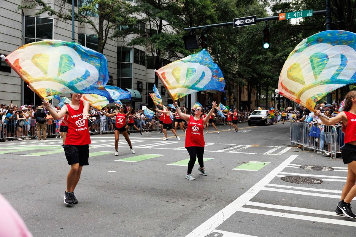 Members of Queen City Twirlers spin colorful flags decorated with Charlotte’s crown symbol during the Charlotte Pride Festival & Parade on Sunday, Aug. 18, 2024