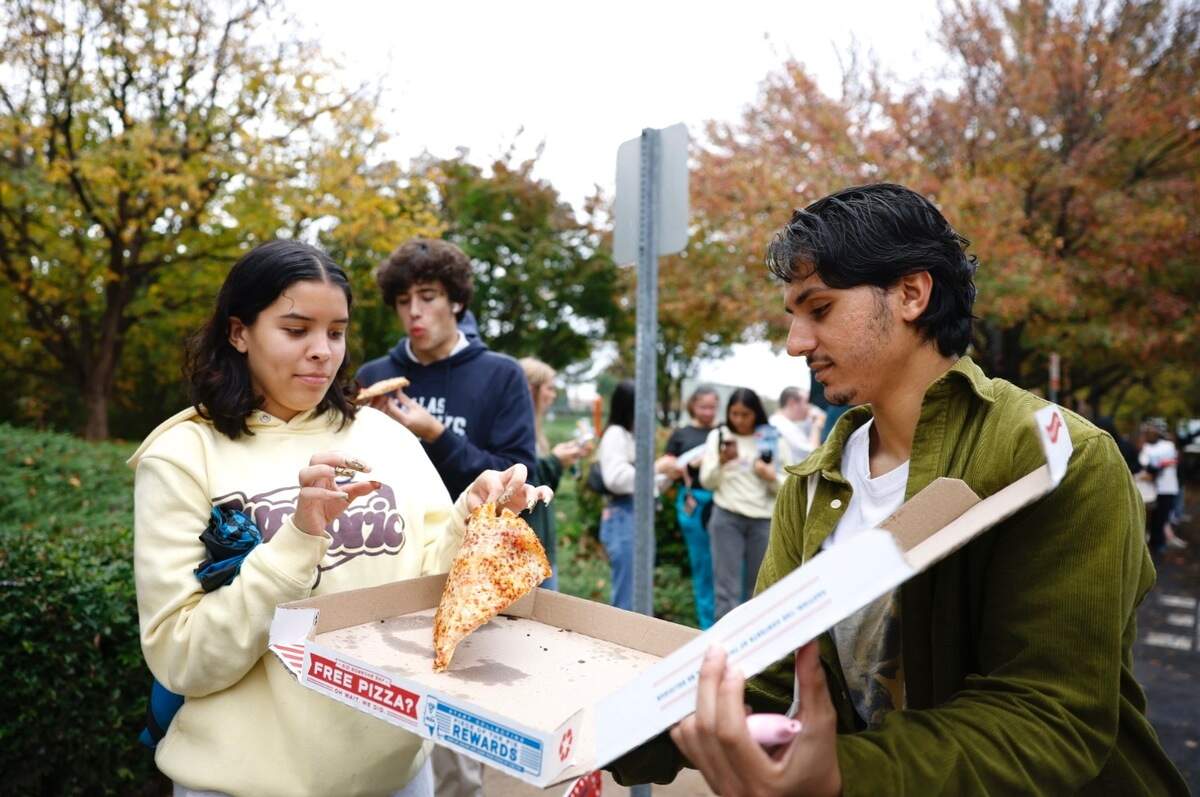 Molly Smith, left, picks up a slice of pizza from Zak Choukri, right, a UNCC student and member of UN-PAC, a non-partisan student organization focused on empowering students, at the Charlotte Mecklenburg Library at University City on Tuesday. Choukri says he knows people are standing in long lines at this location, specifically students, and he wants to make sure they stay fed.