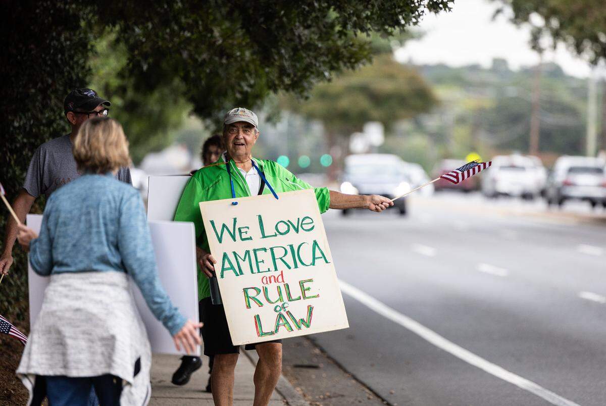 Ken Hungate waves to cars during a non-partisan patriotic march with residents of Southminster retirement community in Charlotte, N.C., on Wednesday, October 8, 2025.