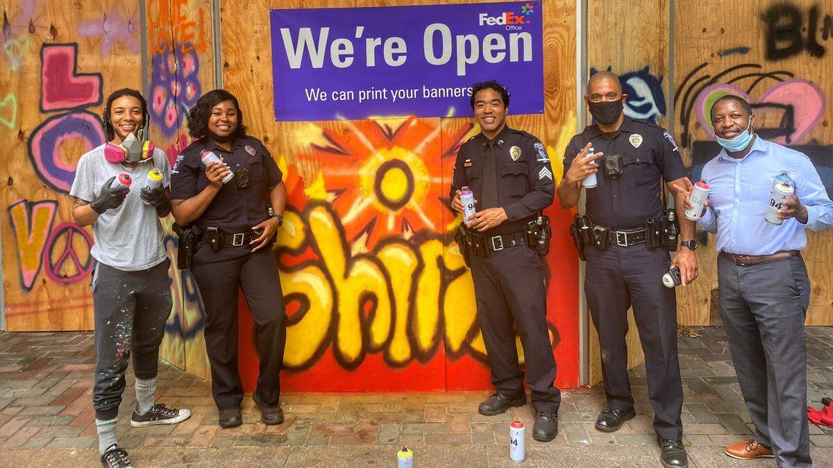 A property management company asked Charlotte Art League to paint over some boarded up windows at one of its North Tryon Street properties. CAL’s offsite exhibit coordinator, Chandler Snipe, saw it as a community project and got CMPD officers involved. Artist DeNeer Davis (far left) showed them how to paint.