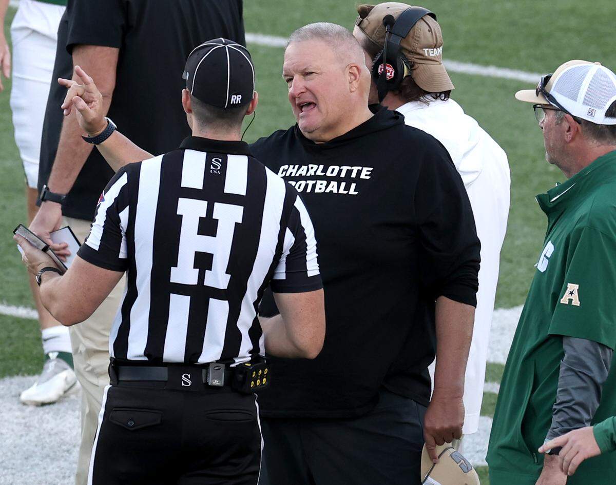 Charlotte 49ers head coach Biff Poggi, center, speaks with Head Line Judge Braden Cox, left, during a break in the action against South Florida on Saturday, November 16, 2024 at Jerry Richardson Stadium.