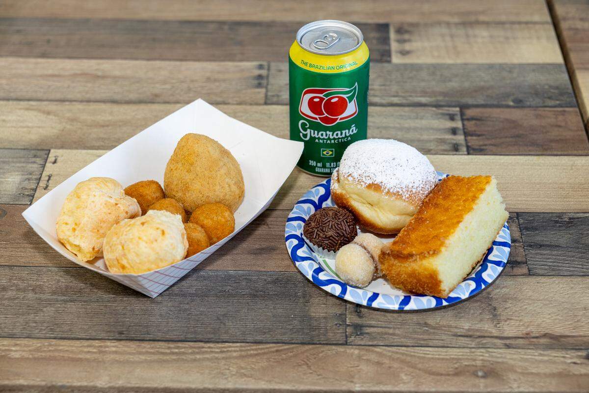 Some food offerings at Tropical Bakery including chicken coxinha, two types of cheese balls, cassava cake, chocolate truffle, a sonho with caramel and Brazilian sodas.