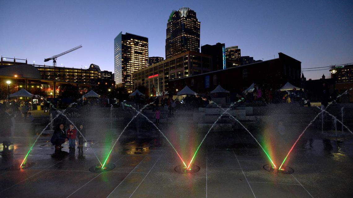 Water jets are illuminated as the uptown Charlotte skyline glows in the background as holiday lights burn for first time in First Ward Park on Tuesday, December 8, 2015.