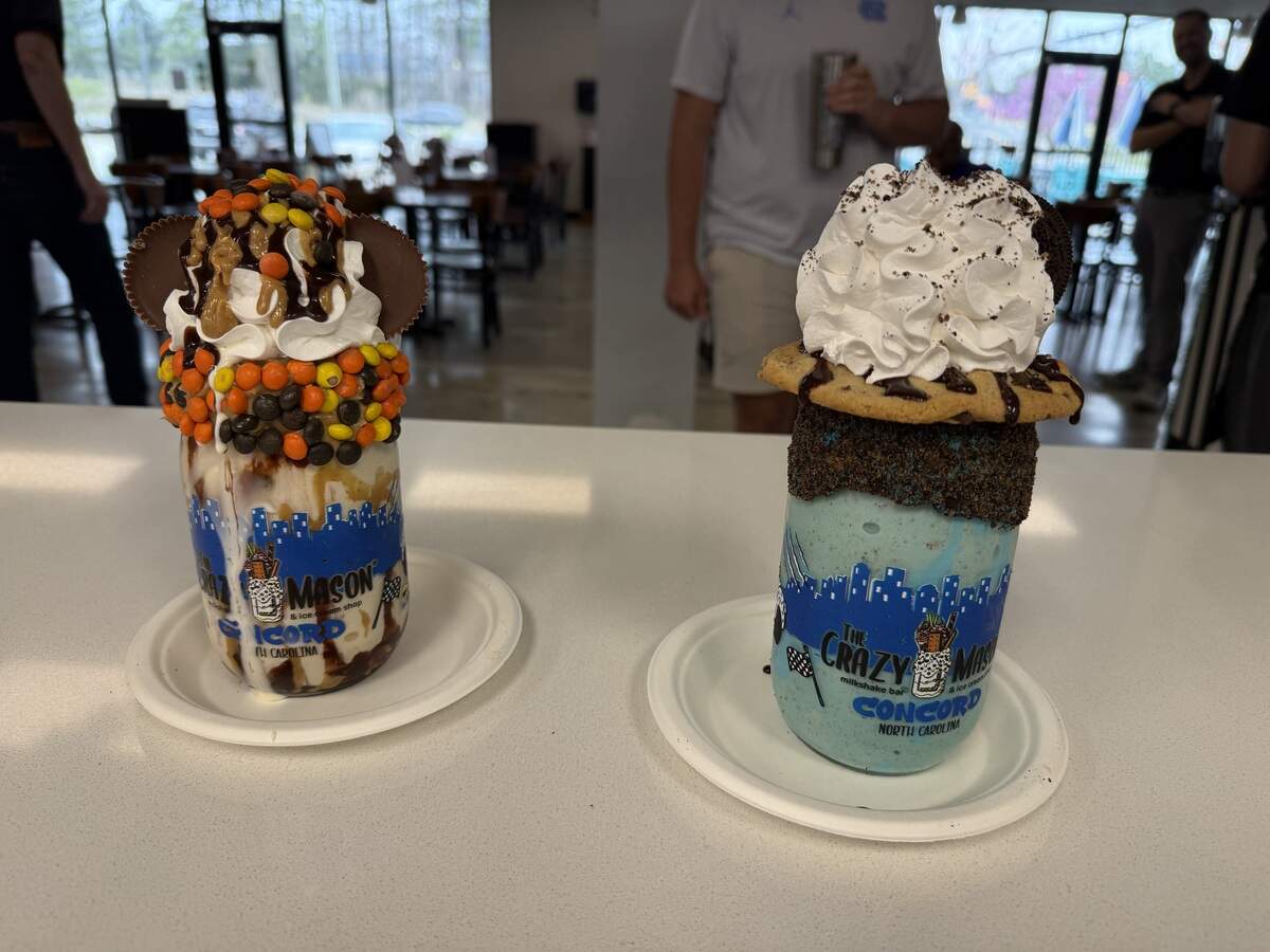 Two elaborate gourmet milkshakes in mason jars topped with whipped cream, cookies, and chocolate candies.