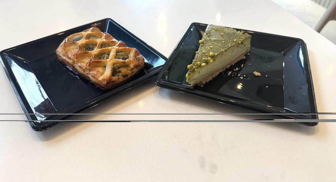 Close-up of two desserts on a white table: a golden-brown lattice-top pastry and a slice of pistachio cheesecake/tart, both served on square black plates.