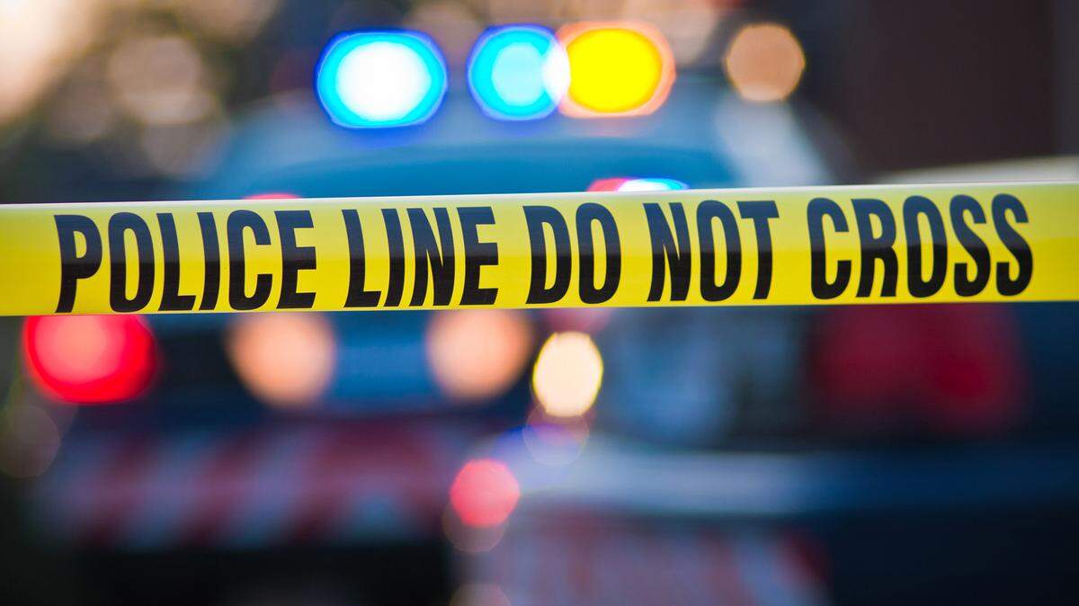 Shallow depth of field image taken of yellow law enforcement line with police car and lights in the background.