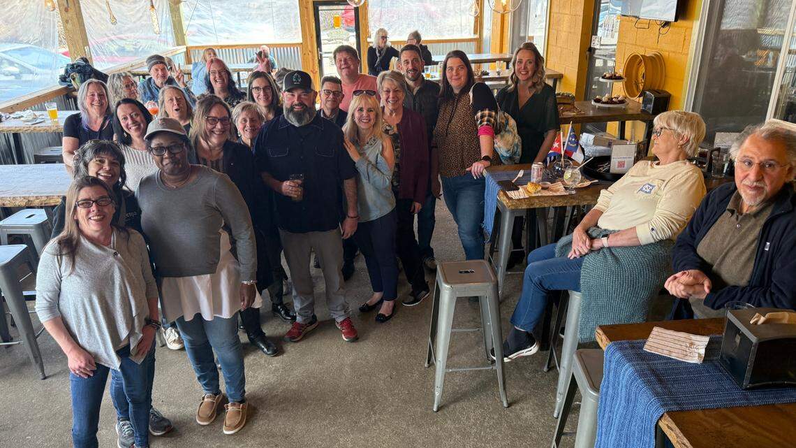 A group shot of approximately half the partygoers including the bearded Tony Prieto, who stands to the left of center, wearing a hat.