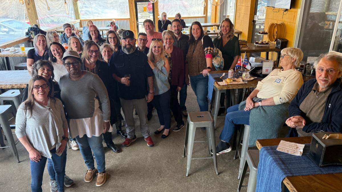 A group shot of approximately half the partygoers including the bearded Tony Prieto, who stands to the left of center, wearing a hat.