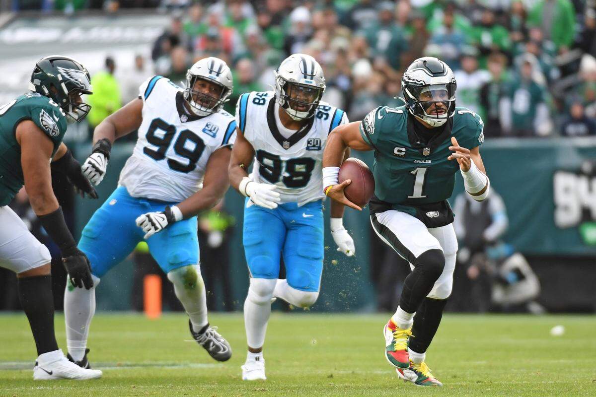 Dec 8, 2024; Philadelphia, Pennsylvania, USA; Philadelphia Eagles quarterback Jalen Hurts (1) runs away from Carolina Panthers linebacker D.J. Wonnum (98) and  defensive tackle Shy Tuttle (99) during the second quarter at Lincoln Financial Field. Mandatory Credit: Eric Hartline-Imagn Images