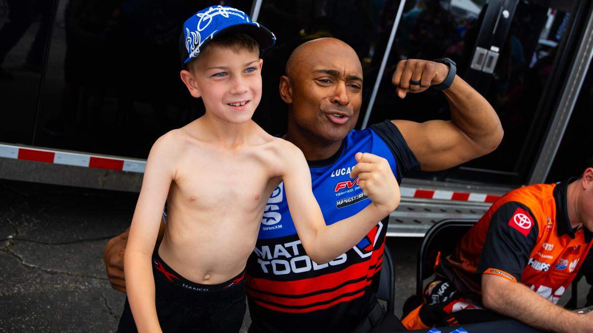 Mar 9, 2024; Gainesville, FL, USA; NHRA top fuel driver Antron Brown (right) flexes alongside a young fan in the pits during qualifying for the Gatornationals at Gainesville Raceway.