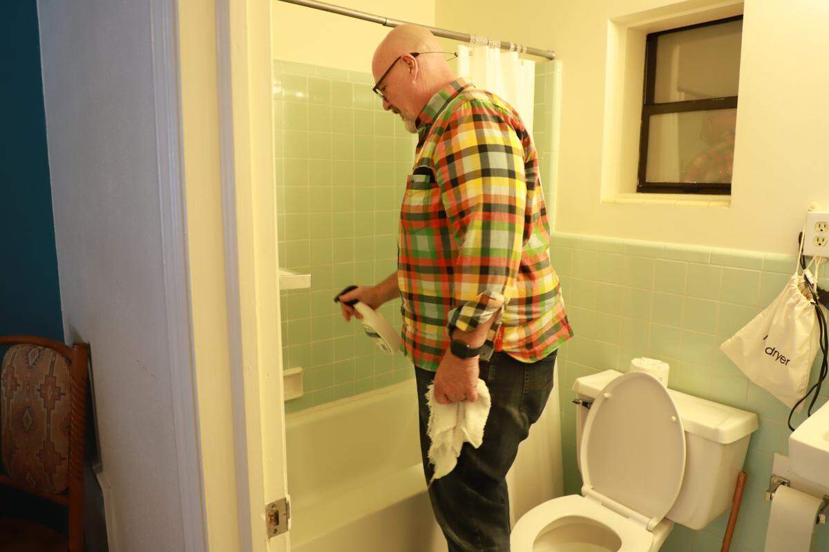 Joseph Franklyn McElroy sprays a bathtub with cleaning solution inside a room at the Meadowlark.