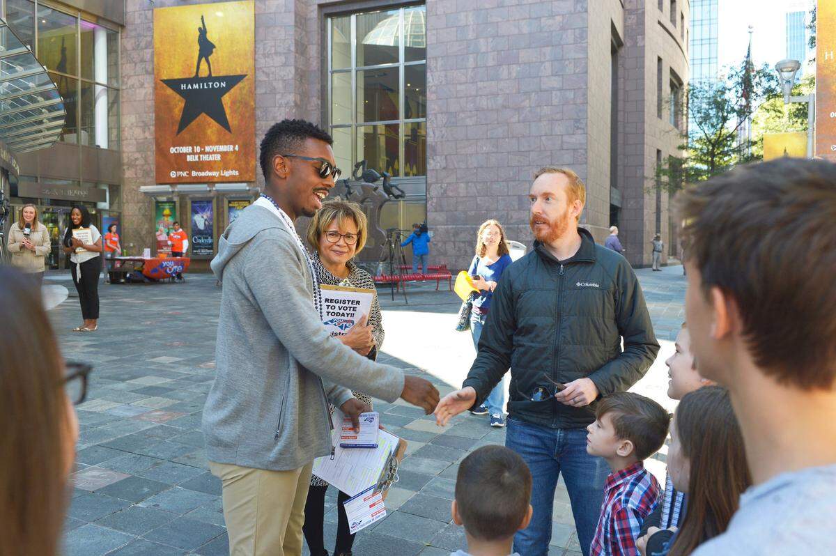 Tyler McKenzie, left, an ensemble member of “Hamilton” who went to Central Academy of Technology and Arts in Monroe, and Charlotte Mayor Vi Lyles shake hands with people during a voter registration drive in front of the Belk Theater Oct. 12. The event was held on the final day to register to vote in NC.