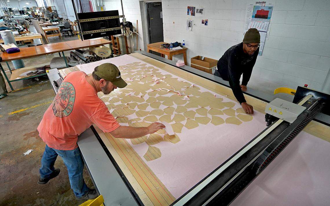 E.J. Victor Furniture lead cutter Andy McClure, left and cutter Shaw Lipsey, right, remove cloth masks from a line on Friday, March 27, 2020. The furniture maker has begun producing medical gowns, mask covers and a triage cot to help in the fight against the Coronavirus.