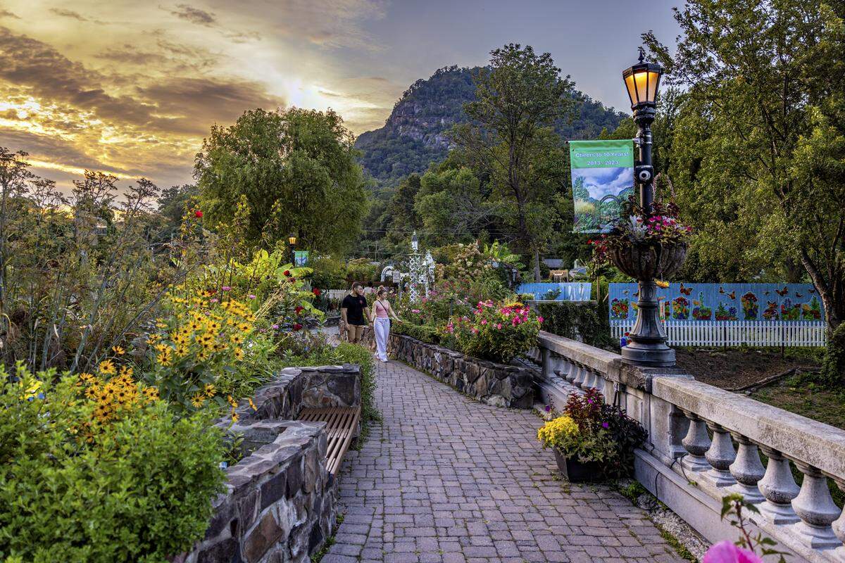 A couple admiring gardens on bridge, surrounded by plants and flowers with mountains in background as the sun begins to set.