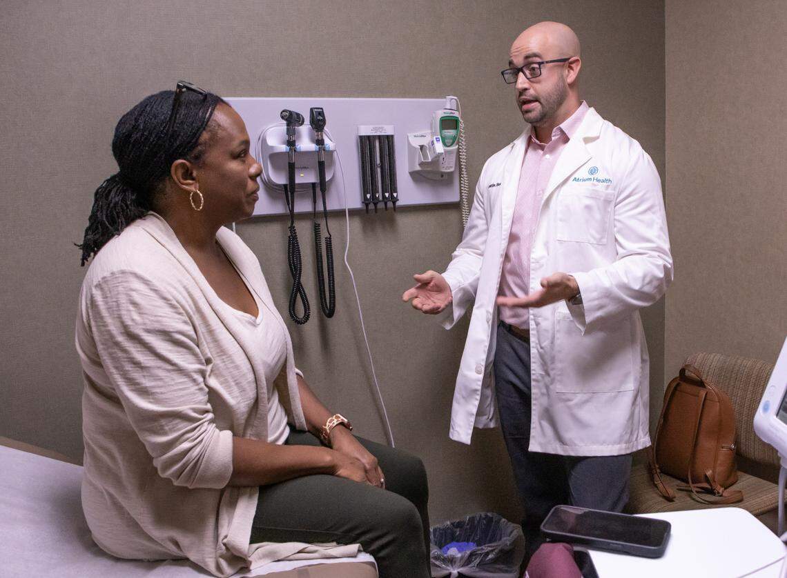 A smartphone sits beside Atrium Health Primary Care Cabarrus Family Medicine Dr. Austin Bush as he meets with patient Valerie Burton. It is using a new AI technology to document the conversation between them, which is synopsized by the program and loaded into the patient’s electronic medical record. Atrium Health is the first health system in the nation to pilot the Nuance Dragon Ambient eXperience Copilot (DAX Copilot), which is designed to free up clinicians to focus on delivering high-quality, personalized care, improve clinical efficiency and reduce administrative workloads.